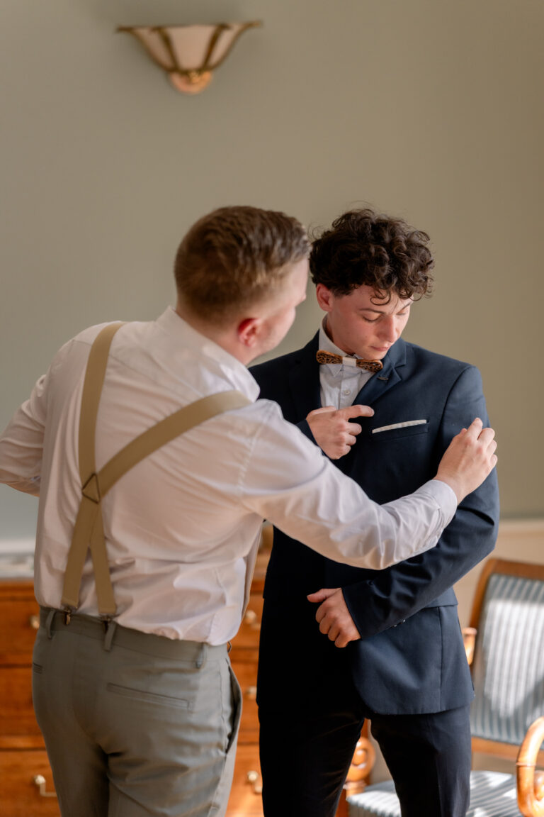 Photographe mariage Jura : marié qui ajuste sa veste avec l’aide d’un proche