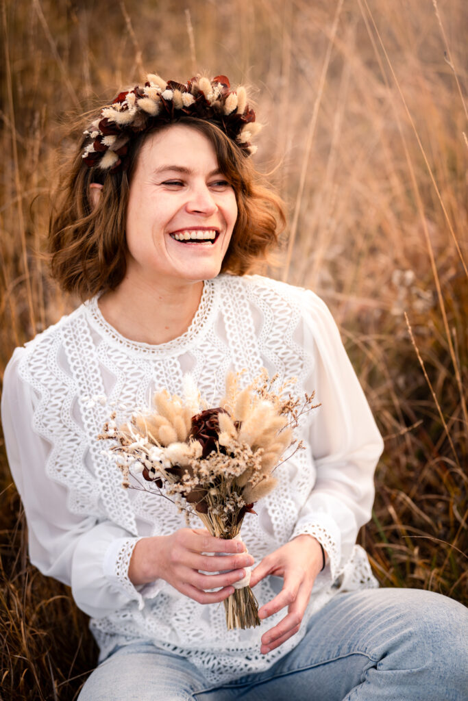 Photographe portrait Morez Jura Genève Lausanne Champagnole Lons-le-Saunier – femme souriante avec couronne de fleurs et bouquet séché dans les herbes hautes