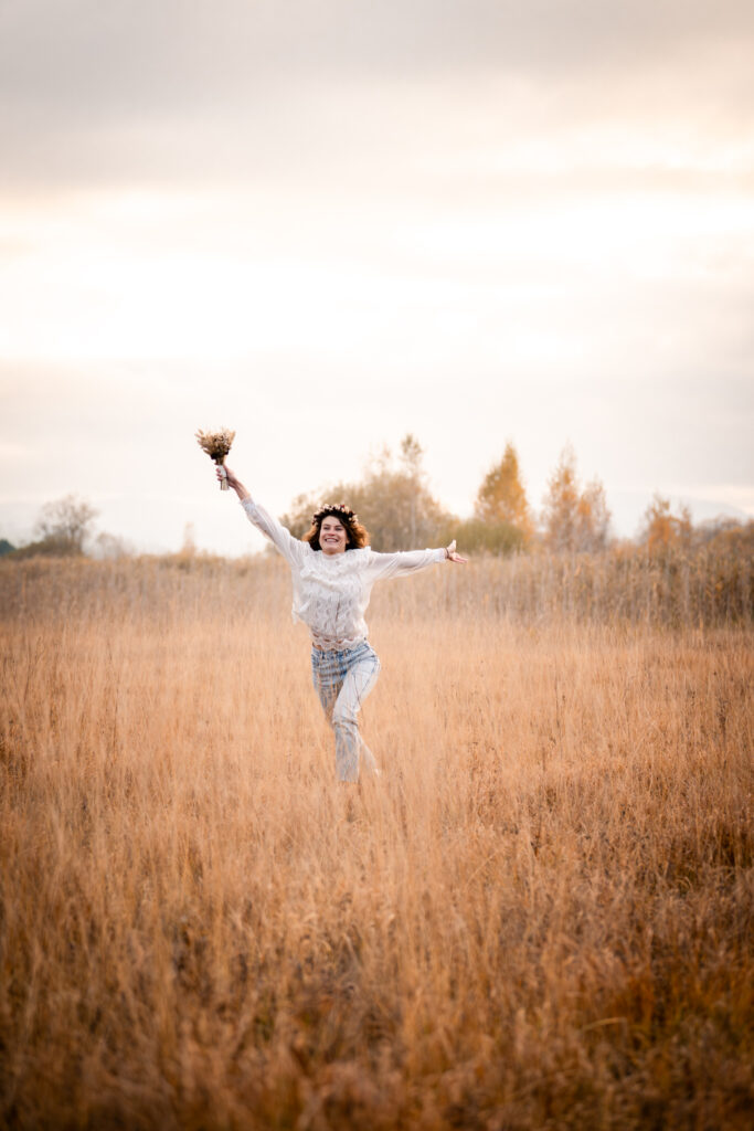 Photographe portrait Morez Jura Genève Lausanne Champagnole Lons-le-Saunier – femme sautant de joie dans un champ d’herbes dorées