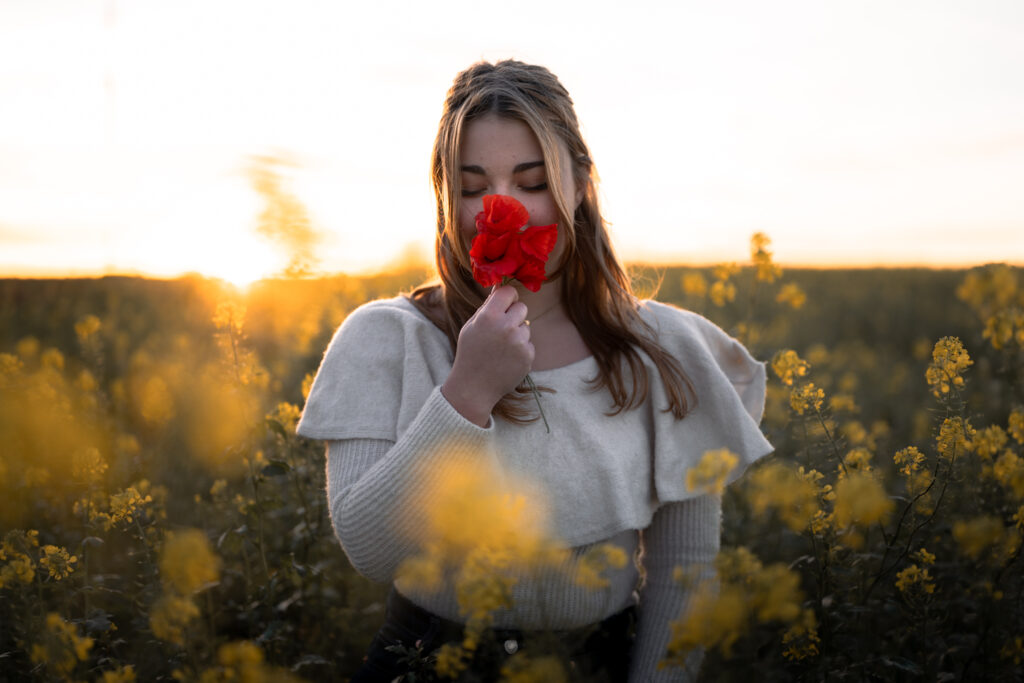 Photographe portrait Morez Jura Genève Lausanne Champagnole Lons-le-Saunier – femme respirant un coquelicot dans un champ de colza au coucher du soleil