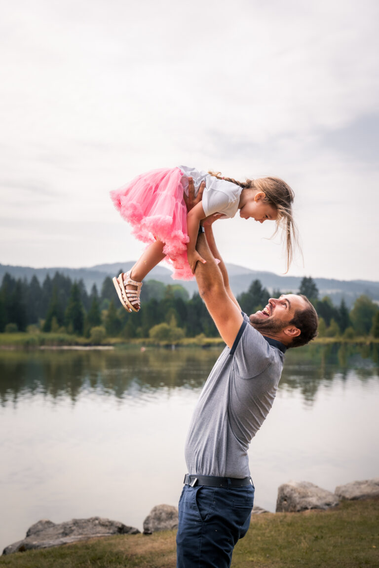 Séance photo famille dans le Haut-Jura : papa faisant voler sa fille au bord d’un lac
