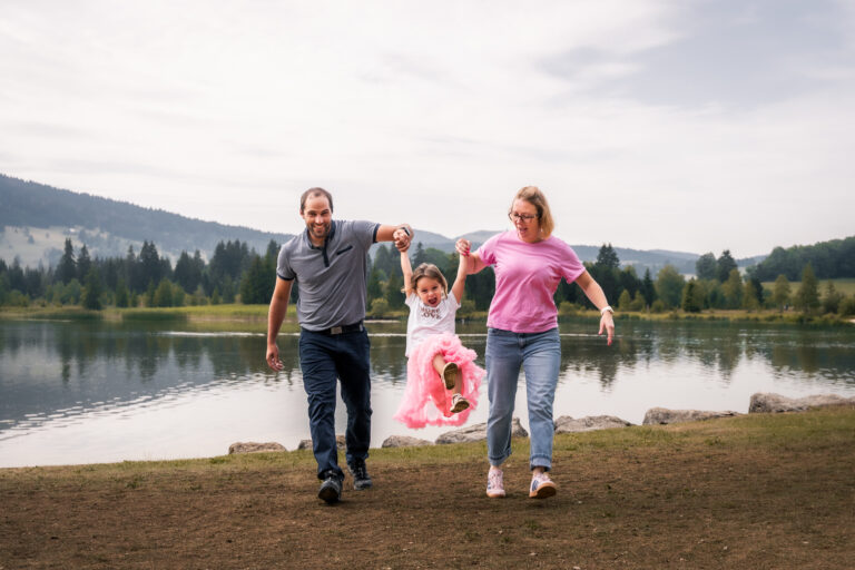 Séance photo famille dans le Haut-Jura : parents faisant sauter leur fille au bord d’un lac