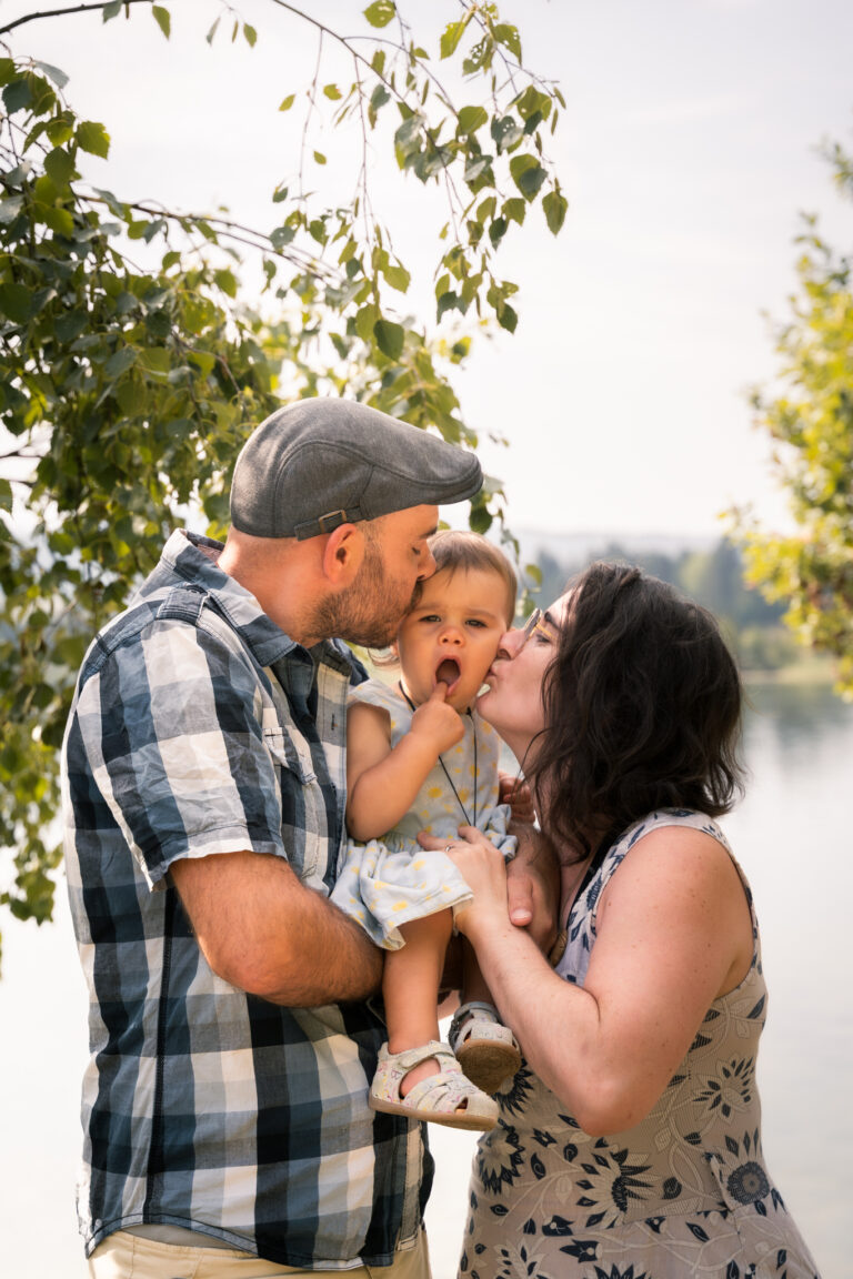 Séance photo famille dans le Haut-Jura : parents faisant un bisou à leur fille au bord d’un lac