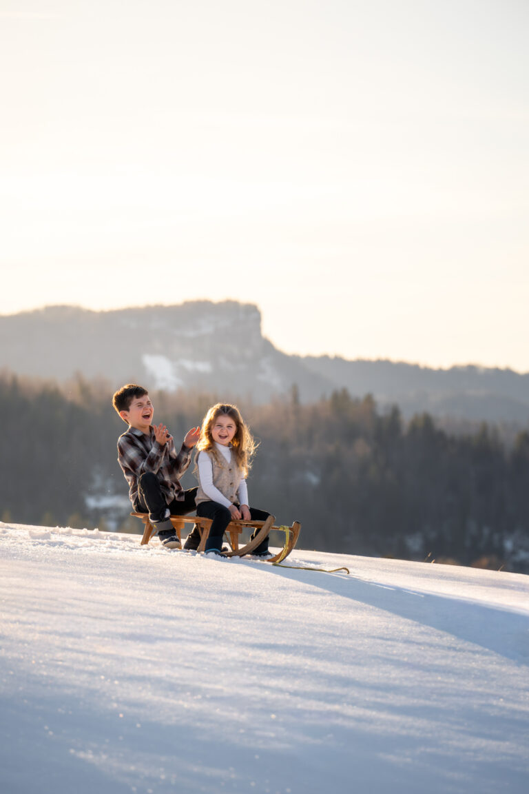 Séance photo famille dans le Jura : deux enfants sur une luge dans la neige de la vallée de Joux