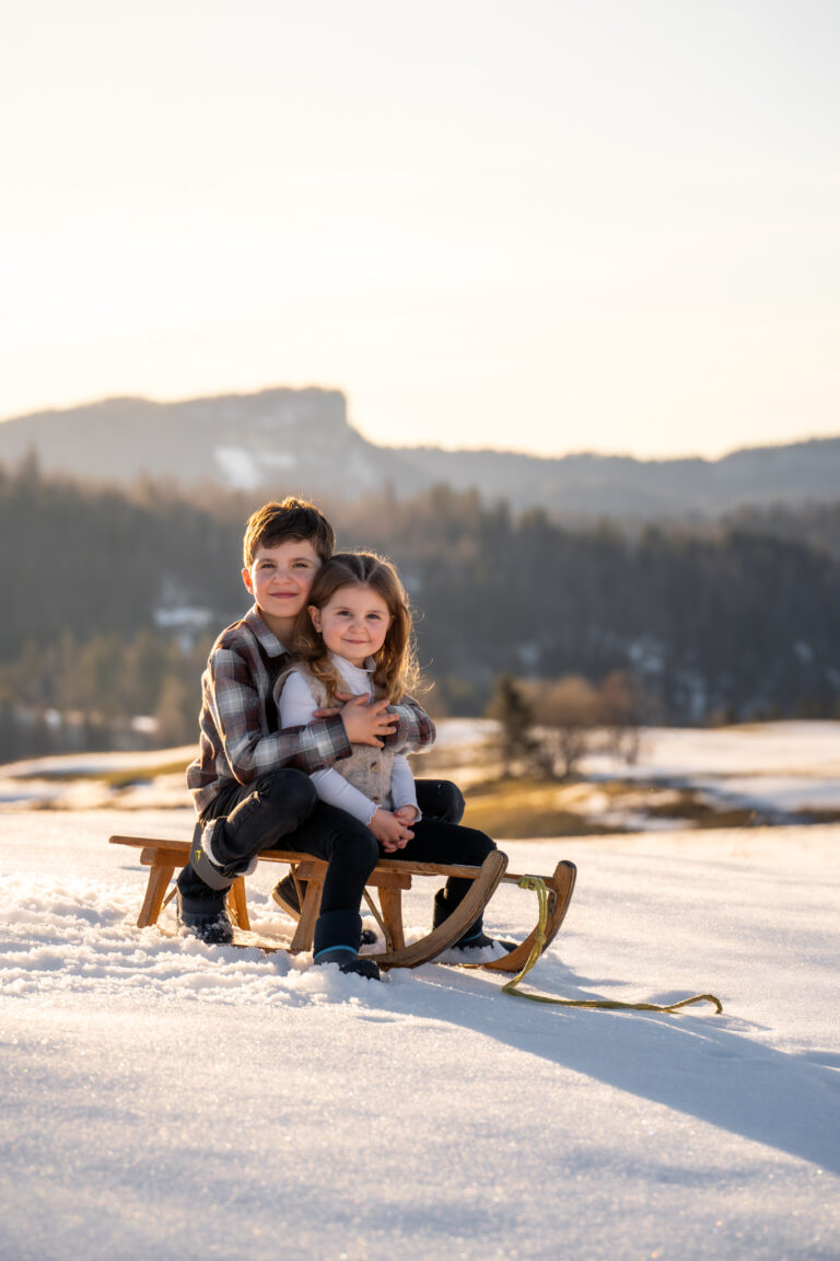 Séance photo famille dans le Haut-Jura : frère et sœur assis sur une luge dans la neige