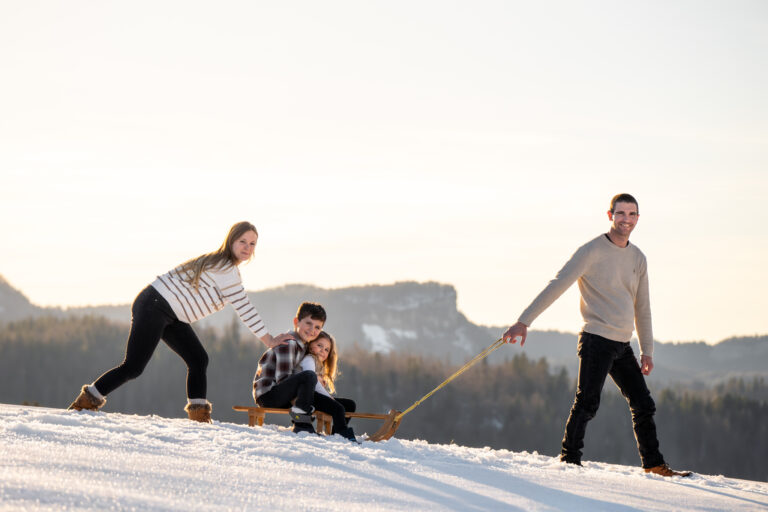 Séance photo famille dans le Haut-Jura : parents tirant leurs enfants en luge dans la neige