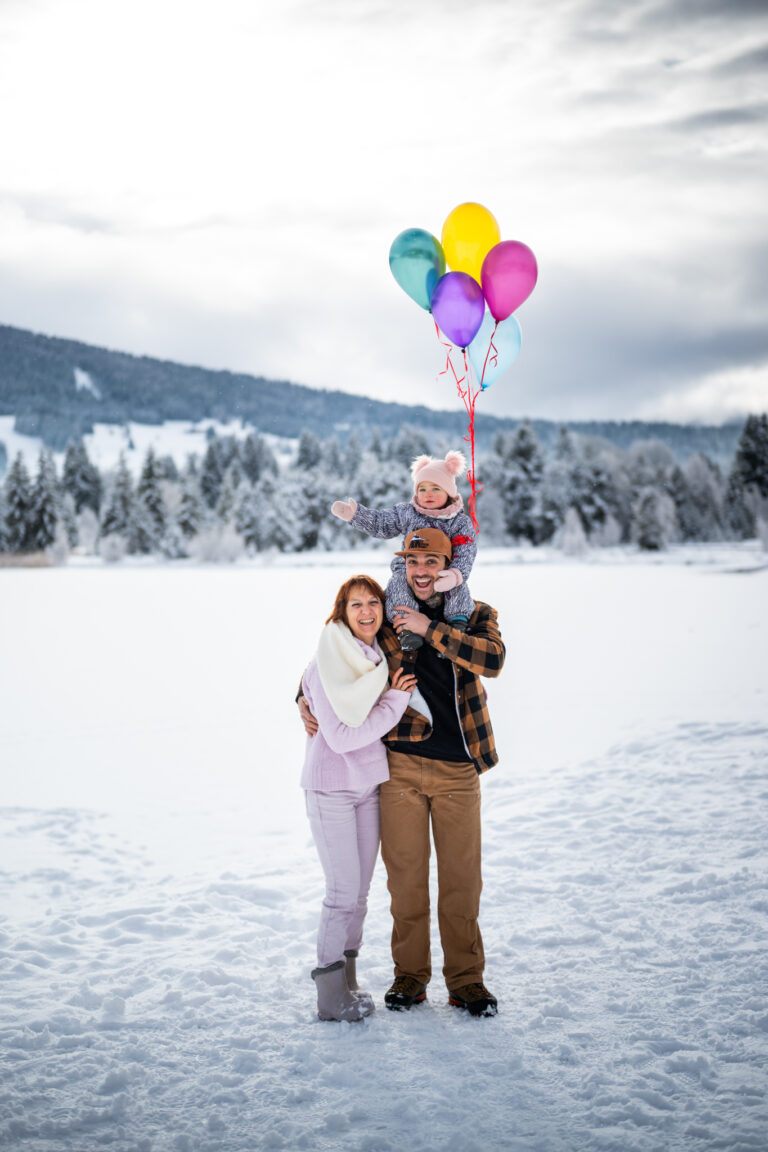 Séance photo famille dans le Haut-Jura : famille avec des ballons colorés dans un paysage enneigé