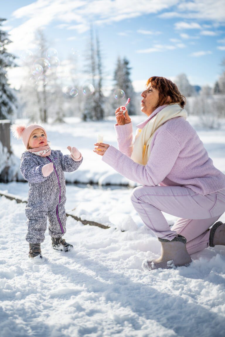 Séance photo famille dans le Haut-Jura : maman et sa petite fille faisant des bulles dans la neige