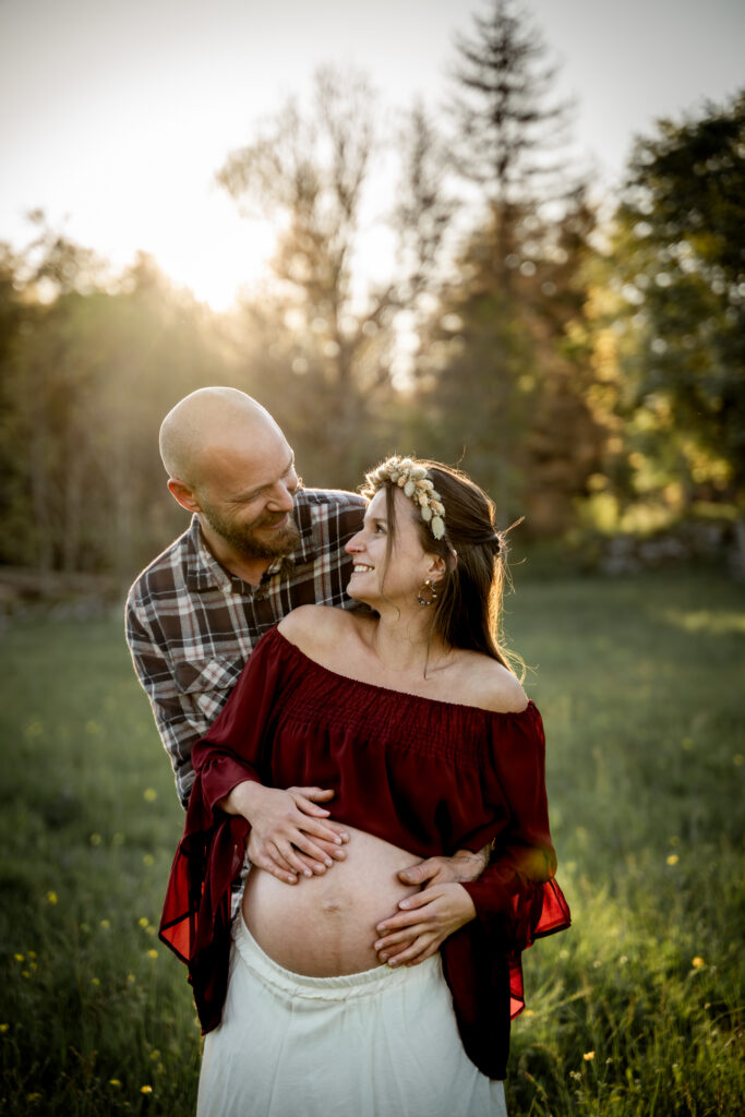 Photographe grossesse Jura – futurs parents enlacés dans un champ au coucher du soleil près de Morez