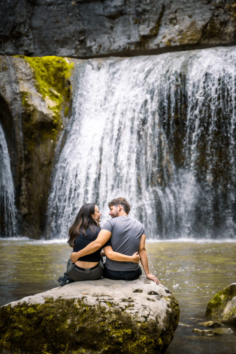 Photographe mariage couple Morez Jura Genève Lausanne Champagnole Lons-le-Saunier Besançon – couple assis sur un rocher face à une cascade