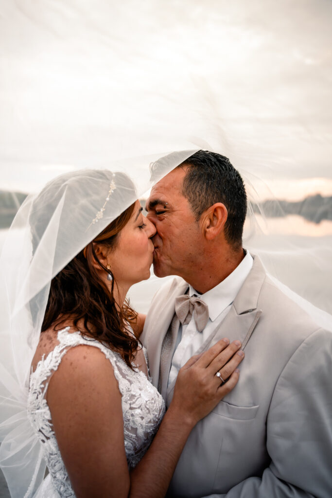 Photographe mariage Jura : marié qui embrasse sa mariée coiffée d’une capeline blanche