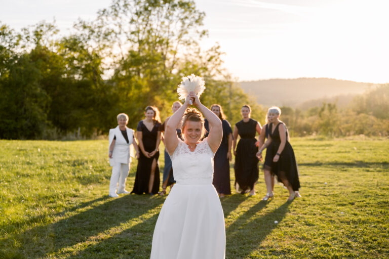 Photographe mariage Jura : mariée qui lance son bouquet dans un pré