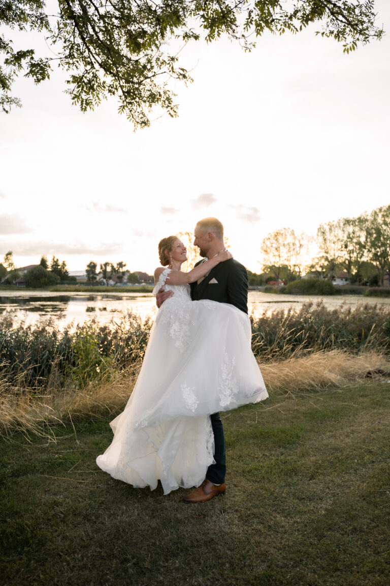 Photographe mariage Jura : marié qui fait tourner sa mariée au bord d’un étang au coucher du soleil