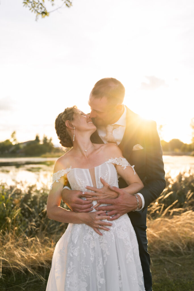 Photographe mariage Jura : mariée en robe de dentelle dans les bras de son marié au soleil couchant