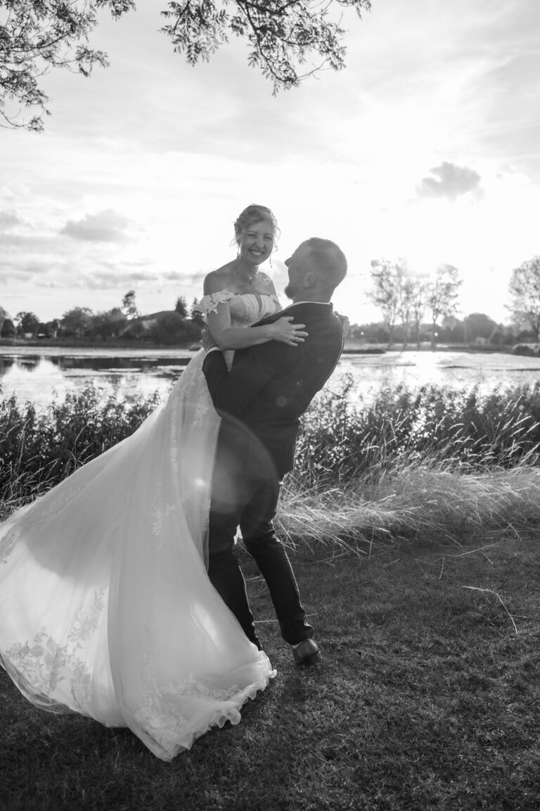 Photographe mariage Jura : marié qui soulève sa mariée dans les herbes, en noir et blanc