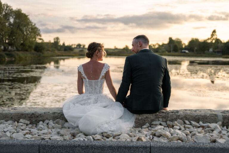 Photographe mariage Jura : mariés assis de dos face au lac au coucher du soleil
