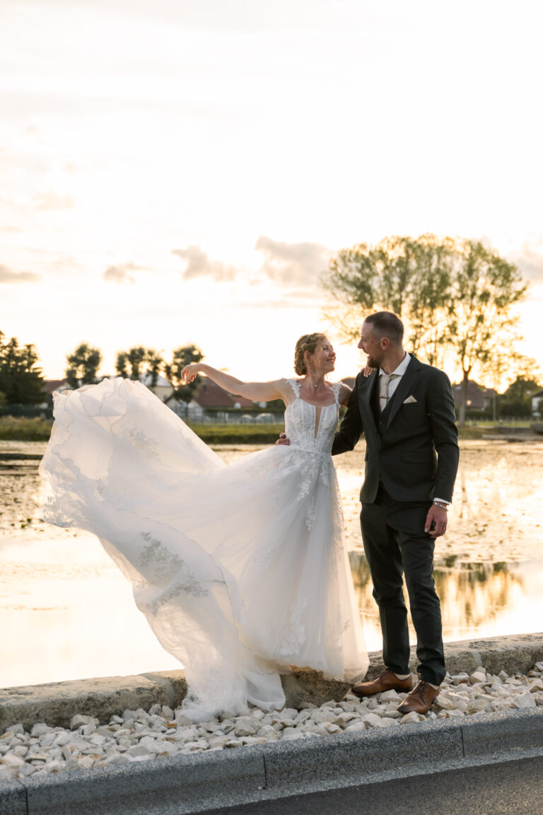 Photographe mariage Jura : mariée qui fait voler sa robe au bord du lac, à côté de son marié