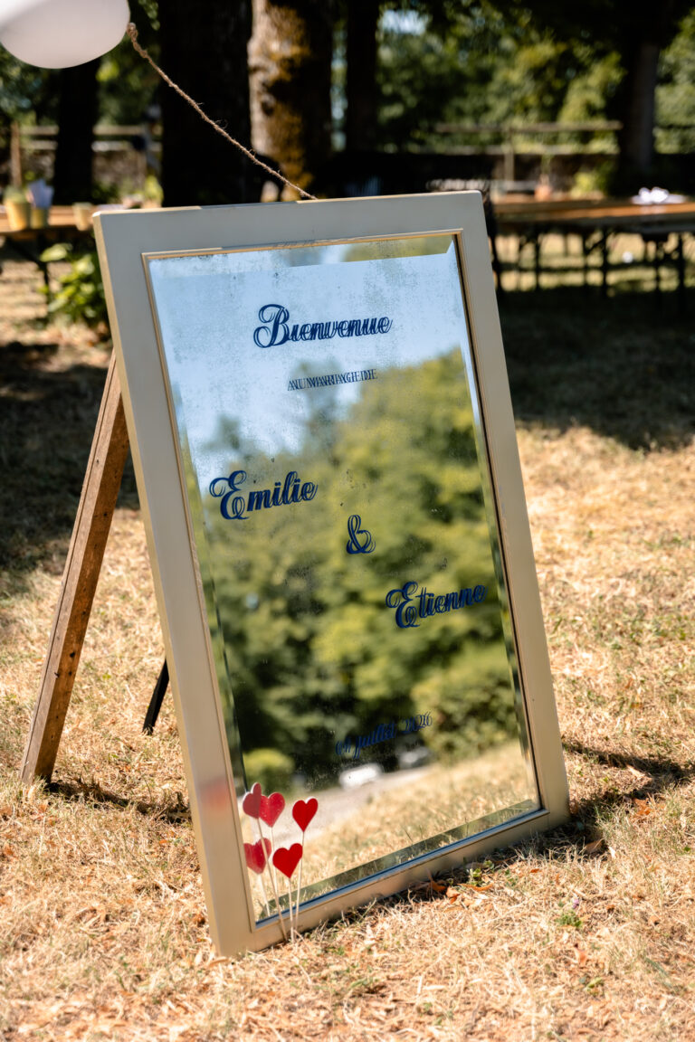 Photographe mariage Jura : miroir de bienvenue posé sur un chevalet dans l’herbe