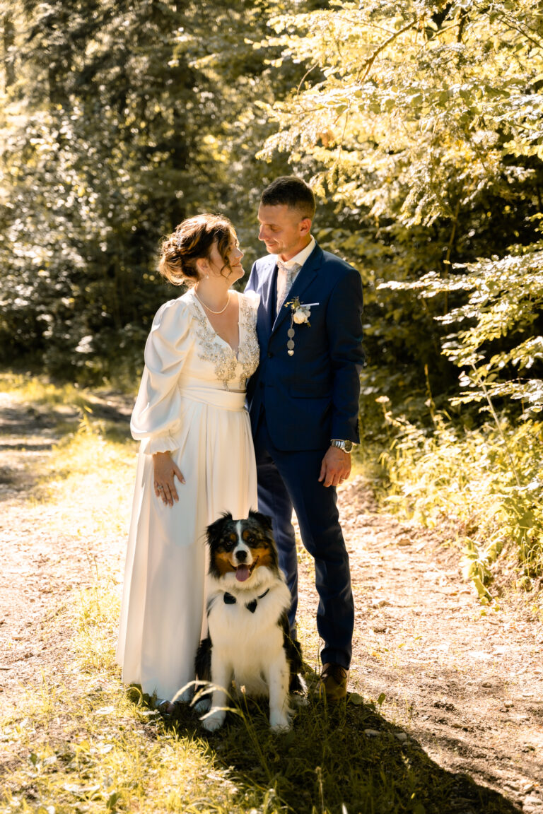 Photographe mariage Jura : mariés et leur chien sur un chemin forestier ensoleillé