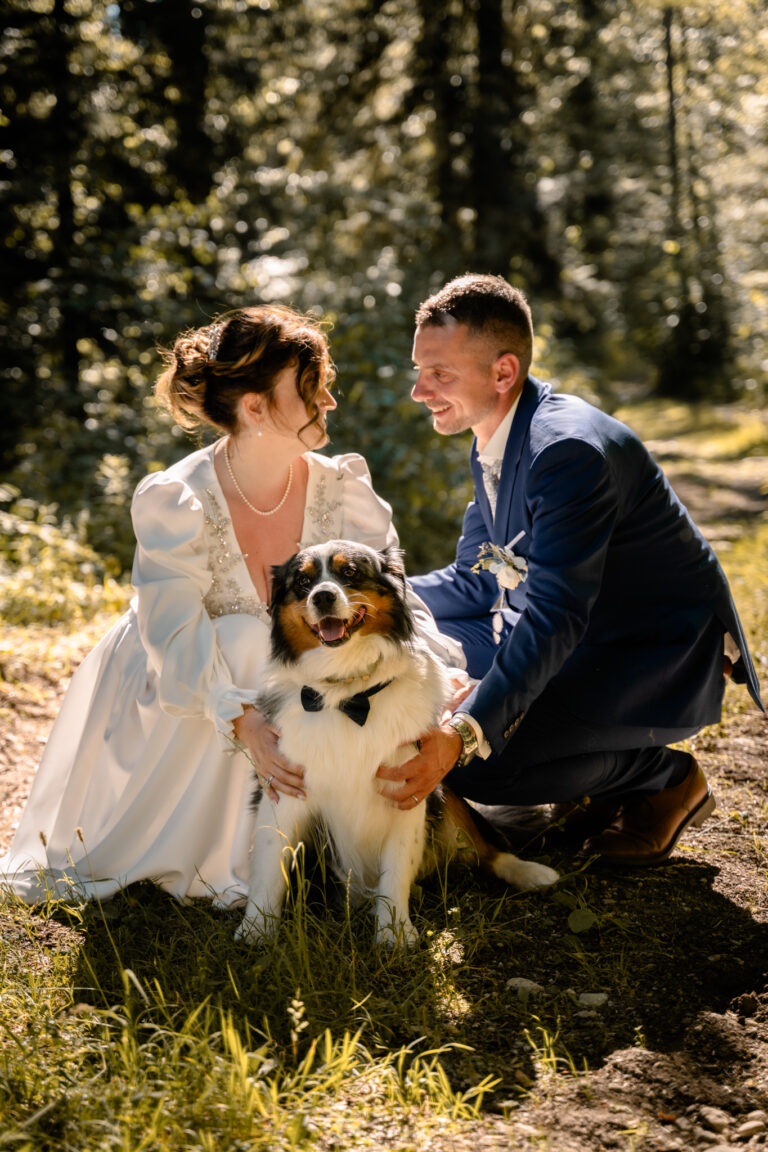 Photographe mariage Jura : mariés accroupis avec leur chien dans l’herbe