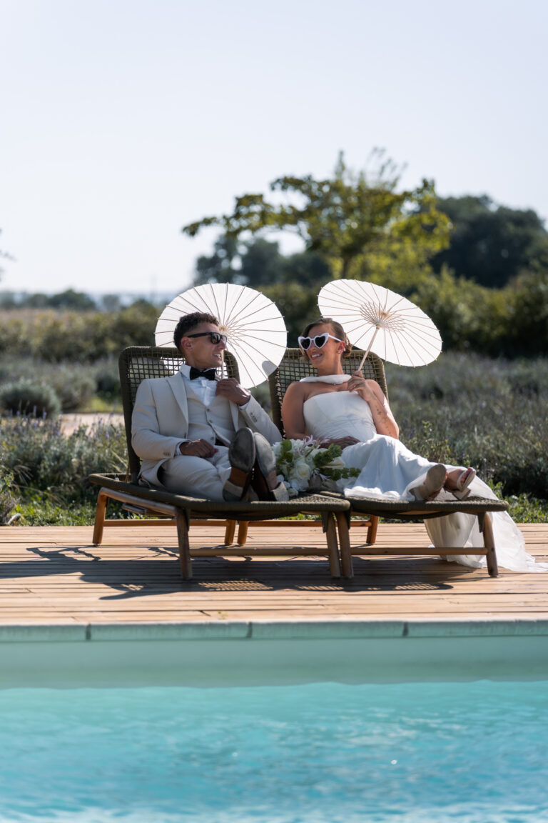 Photographe mariage Jura : mariés qui trinquent sur des transats au bord de la piscine, dans la Drôme