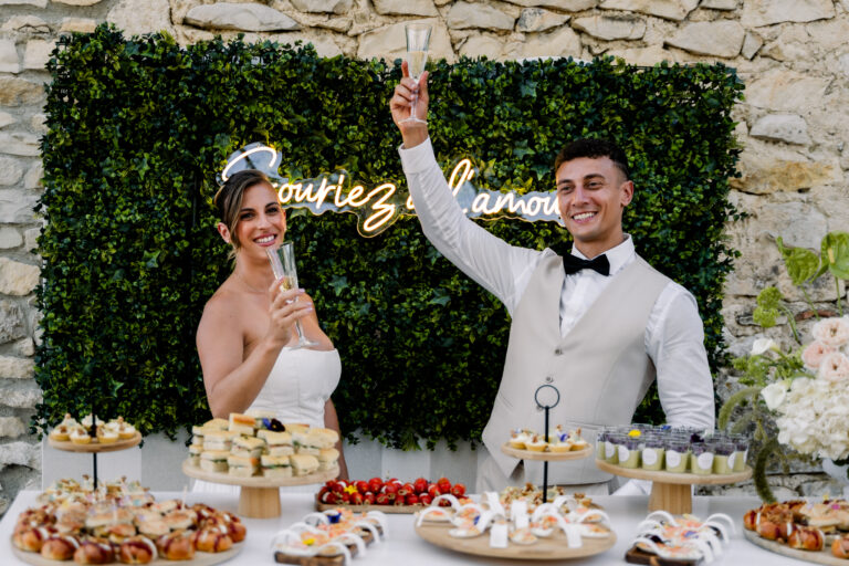 Photographe mariage Jura : mariés qui lèvent leur verre devant un mur végétal