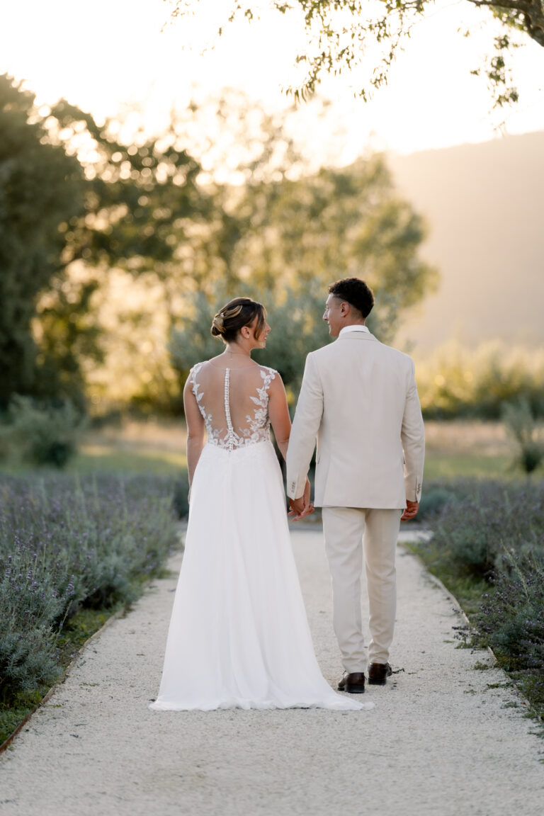 Photographe mariage Jura : mariés qui marchent main dans la main dans une allée de lavande