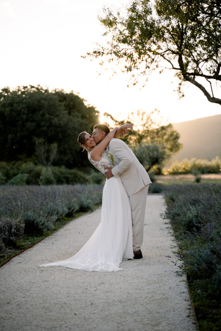 Photographe mariage Jura : marié qui fait basculer sa mariée dans une allée bordée de lavande