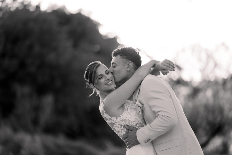 Photographe mariage Jura : marié qui enlace sa mariée par derrière, en noir et blanc