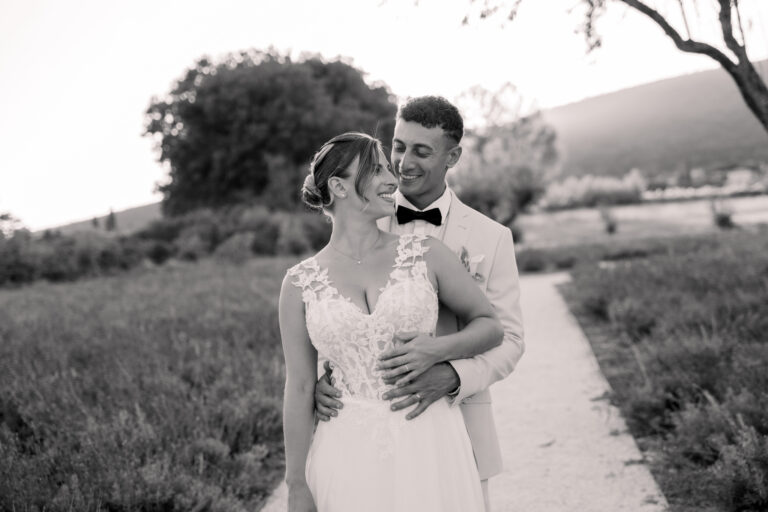 Photographe mariage Jura : mariée qui serre le bras de son marié dans un jardin de lavande, en noir et blanc