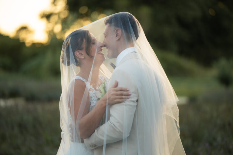 Photographe mariage Jura : mariée voilée enlacée par son marié dans une lumière dorée
