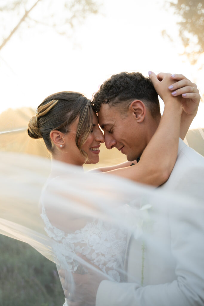 Bride with a flowing veil embracing her groom, foreheads touching and smiling, romantic wedding couple portrait in the Drôme, France