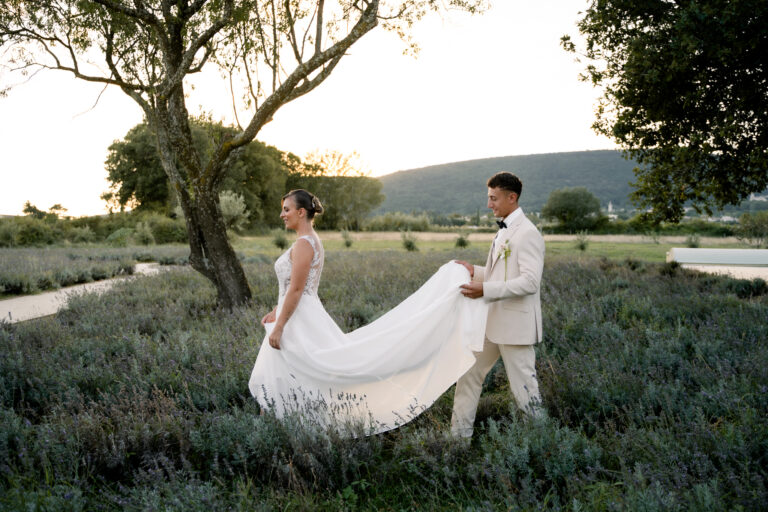 Photographe mariage Jura : mariée qui soulève sa robe en marchant avec son marié dans les lavandes