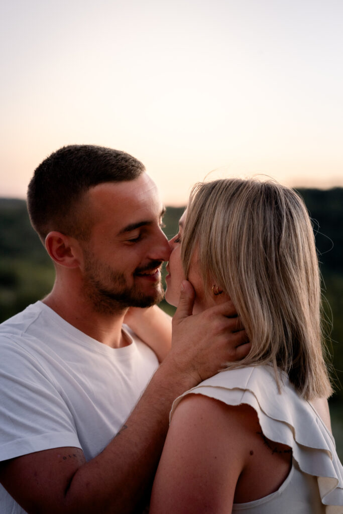Couple about to kiss at sunset, his hand gently on her cheek, engagement session in the Jura mountains near Geneva