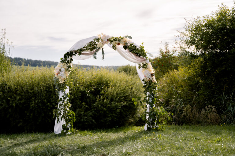 Photographe mariage Jura : arche fleurie dressée dans un jardin pour la cérémonie laïque