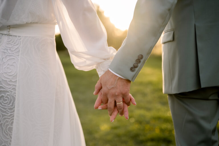 Photographe mariage Jura : mains des mariés qui se tiennent à contre-jour