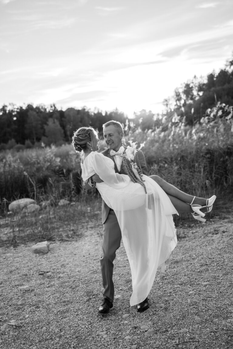 Photographe mariage Jura : marié qui soulève sa mariée au bord de l’eau, en noir et blanc