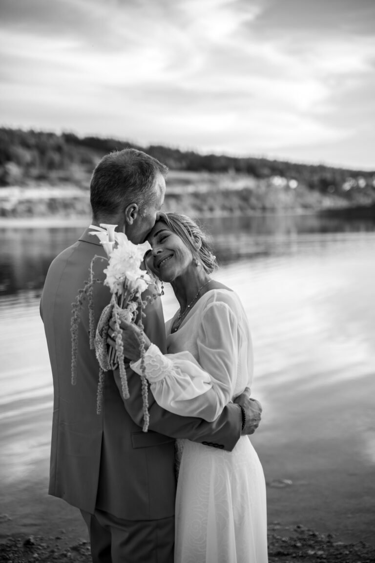 Photographe mariage Jura : mariés tendrement enlacés au bord du lac, en noir et blanc