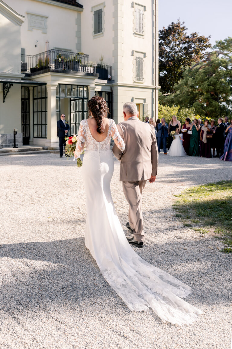 Photographe mariage Jura : mariée qui arrive au bras d’un proche devant le Château de Crissier