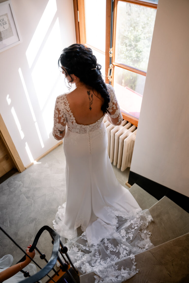 Photographe mariage Jura : mariée de dos dans sa robe, près de la fenêtre