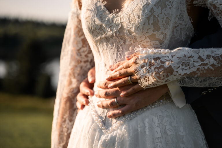 Photographe mariage Jura : mains du marié sur la robe en dentelle de la mariée