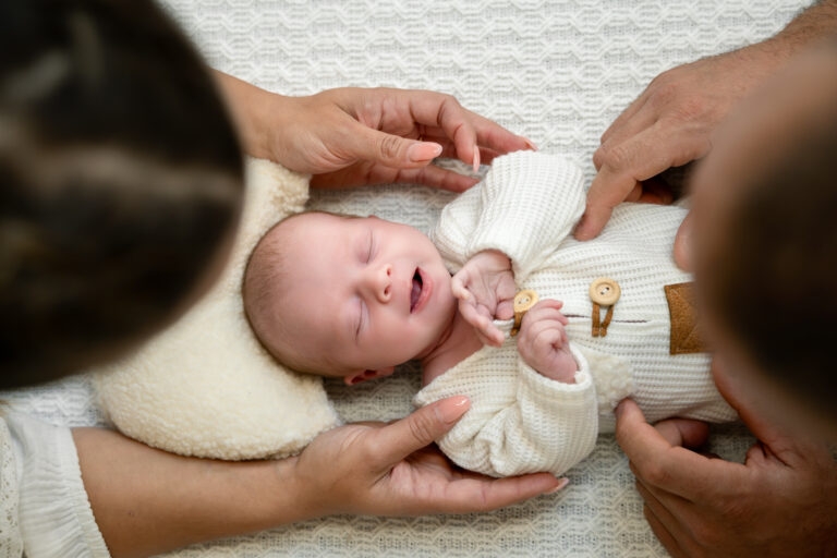 Photographe naissance Jura Morez – bébé allongé, mains des parents autour de lui